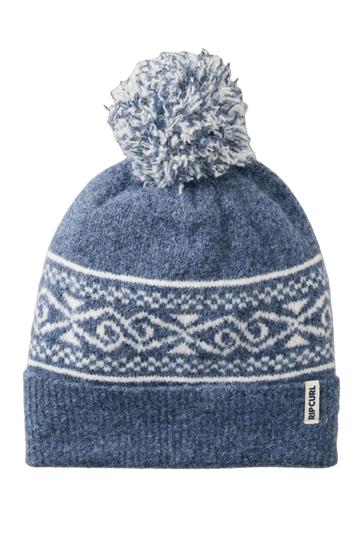 The Rip Curl Cosmic Kiss Jacquard Beanie is blue with a white geometric pattern, folded brim, fabric "RIP CURL" tag, and a large pom-pom—ideal for stylish winter wear.