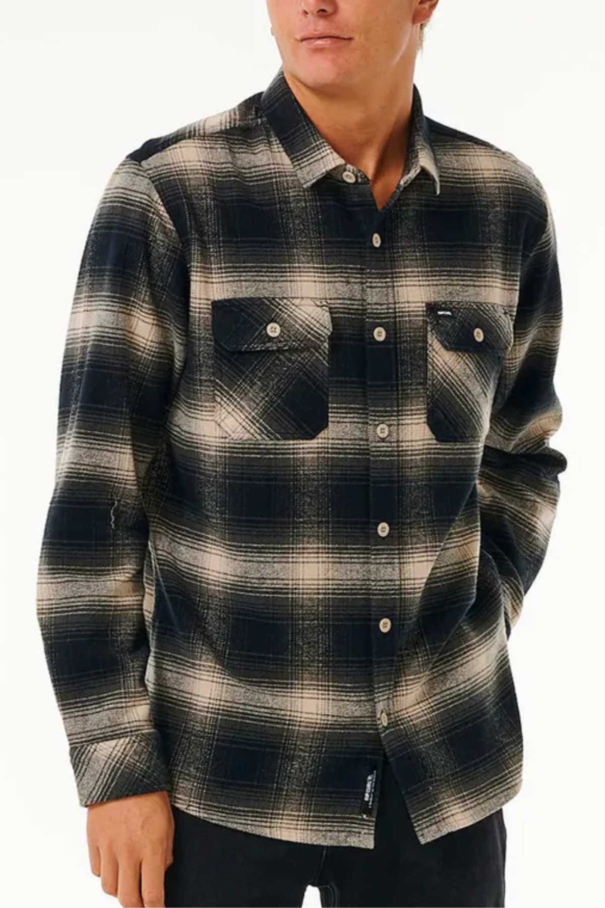 Someone stands against a plain white background wearing the Rip Curl Count Flannel Shirt, a black and beige plaid long-sleeve cotton flannel featuring two chest pockets.