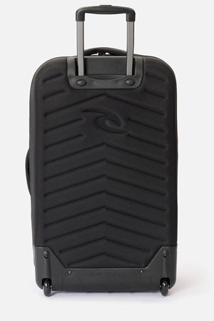 The Rip Curl F-Light Global 100L is a black hard-shell roller bag with a telescopic handle, two wheels, diagonal textured lines, an embossed Rip Curl logo, and a built-in AirTag sleeve for extra travel security.