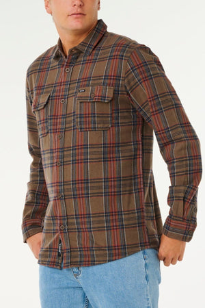 A person wearing a Rip Curl Griffin Flannel Shirt—men's brown and red cotton flannel with chest pockets—paired with blue jeans, stands against a plain white background.