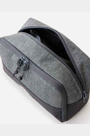The Rip Curl Groom Classic Surf Toiletry Bag, in a gray hue with a zippered closure, is partially open to reveal its roomy interior. This eco-friendly design includes two zipper pulls and a textured fabric, enhanced by a darker base for contrast, and is displayed against a plain white background.