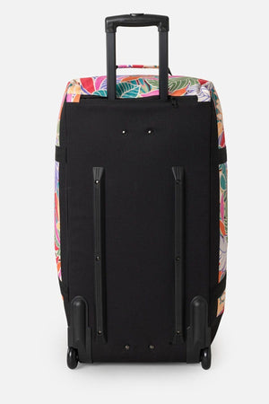 The Rip Curl Jupiter 80L Mixed Travel Bag, made of recycled polyester, stands upright with its black wheeled design and vibrant floral pattern on the sides and top. It features an extended telescopic handle and rests smoothly on two small wheels against a plain white background.