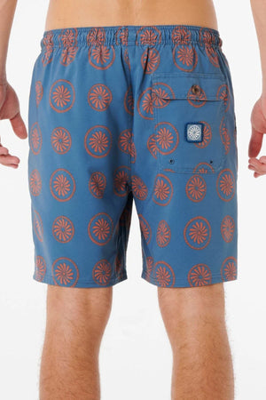 A person is shown from the waist down, wearing Rip Curl Mod Cali Volley Shorts in blue with an orange circular geometric pattern. These quick-dry shorts include a buttoned back pocket and a small label, set against a plain white background.