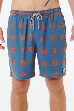 A person wears Rip Curl Mod Cali Volley Shorts in blue with an orange circular pattern, a white drawstring, and a small left-leg patch. Made from quick-dry fabric. The photo is cropped from mid-torso to above the knees.