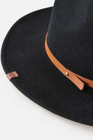 The Rip Curl Nevada Wool Panama is a black wide-brimmed hat made of wool felt, accented with a brown leather headband with a gold stud and loop detail. Its slightly upturned brim adds flair, set against a plain white background.