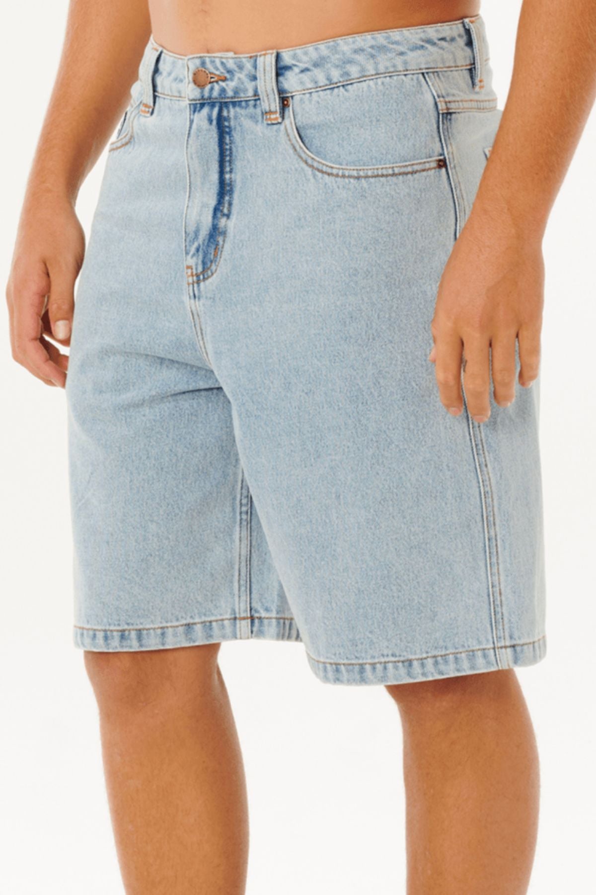Someone wears the Rip Curl Nu Dose Denim Walkshort in light blue, featuring a baggy fit, front and back pockets, a button and zipper fly, ending just above the knees, while standing against a plain white background.