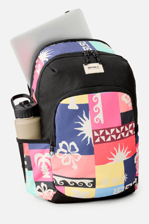 The Rip Curl Ozone 2.0 30L Backpack displays abstract pink, blue, yellow, and black patterns, with a front zip pocket, a water bottle in the side pocket, and a laptop partly inside the main compartment.