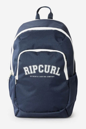 The Rip Curl Ozone 2.0 30L Backpack is navy blue with white accents, made from recycled polyester. It has "RIP CURL AUTHENTIC SURFING COMPANY" on the front, a top handle, laptop section, front zip pocket, and side pockets.
