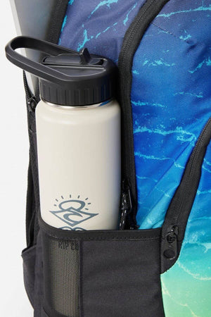 A white water bottle with a black lid sits in the side mesh pocket of a blue and green Rip Curl Ozone 30L Faded Slant Backpack, featuring organiser pockets and a dedicated laptop section for convenience.