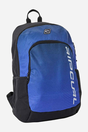 The Rip Curl Ozone 30L School Backpack showcases an eye-catching geometric pattern on its front pocket in blue and black. Made from recycled polyester, it provides a 30L capacity and includes two main compartments with adjustable shoulder straps. The brand logo is vertically displayed in white on the front.