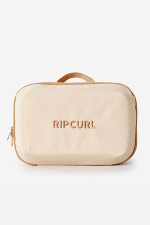 The Rip Curl Ultimate Beauty Case is a rectangular beige beauty case made from recycled polyester, featuring a zipper, small top handle, internal mesh organiser, and "RIP CURL" embroidered on the front.