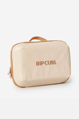 The Rip Curl Ultimate Beauty Case is a beige rectangular case with a tan zipper and handle, "RIP CURL" in brown on the front. Made from recycled polyester, it features an internal mesh organiser for easy storage.