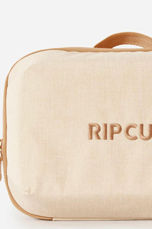 The Rip Curl Ultimate Beauty Case is a beige, rectangular bag made from recycled polyester, featuring a zipper, handle, internal mesh organiser, and "RIP CURL" embroidered on the front.