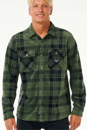 A person with light hair is wearing a green and black plaid Rip Curl Party Pack Polar Fleece Shirt made of recycled polyester, featuring two chest pockets. They have paired it with black pants against a white background.