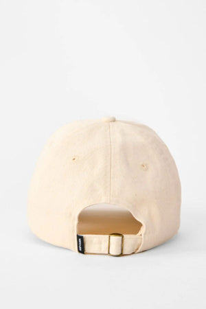 The Rip Curl Premium Surf Cap in beige cotton twill is shown from the back, displaying a fabric strap with metal buckle for size adjustment and a small black tag. The background is plain white.