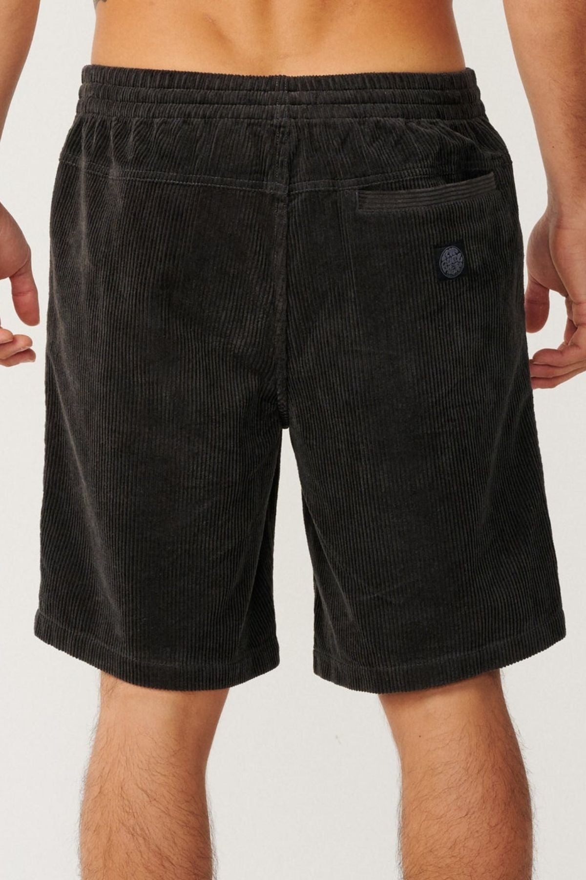 A person is seen from the back wearing Rip Curl Premium Surf Cord 19" Volley shorts in black, featuring an elastic waistband, a back pocket, and a patch above the pocket.