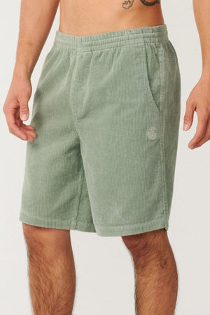 A person wearing Rip Curl Premium Surf Cord 19" Volley shorts in light green, made of cotton with an elastic waistband and side pockets. Ideal for water sports, the shorts feature a small circular logo on the left thigh. The upper body and face are not visible.