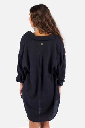 A woman with long, wavy brown hair stands facing away from the camera in a loose-fitting black Rip Curl Premium Surf Holiday Shirt. Her silhouette graces the plain white background, capturing an effortless style.