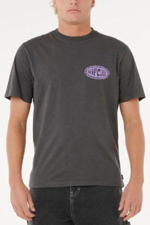 A person wears the Rip Curl Raw Energy De Oval Teeβa plain black short-sleeve shirt with a small purple Rip Curl logo on the left chestβstanding against a white background.