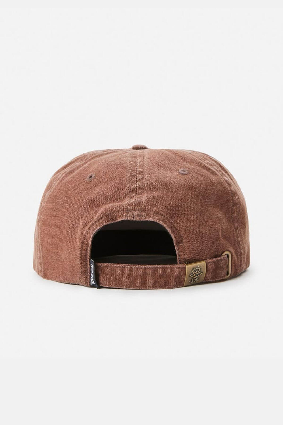 The brown, weathered Rip Curl Searchers Canvas Cap is shown from the back, featuring an adjustable strap with a brass buckle. A small tag is on the left side and a subtle embroidered logo graces the buckle. It rests against a plain, light gray background.