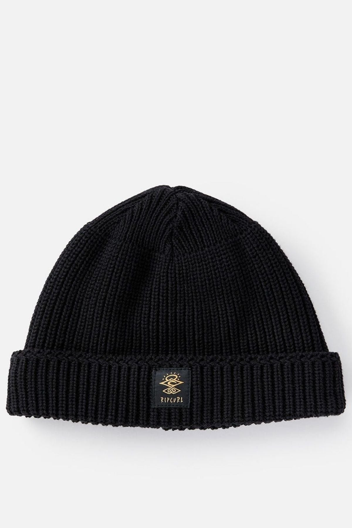 The Rip Curl Searchers Regular Beanie is a black, ribbed knit hat with a folded brim and a small gold-embroidered logo patch on the front center, shown laid flat on a light background.