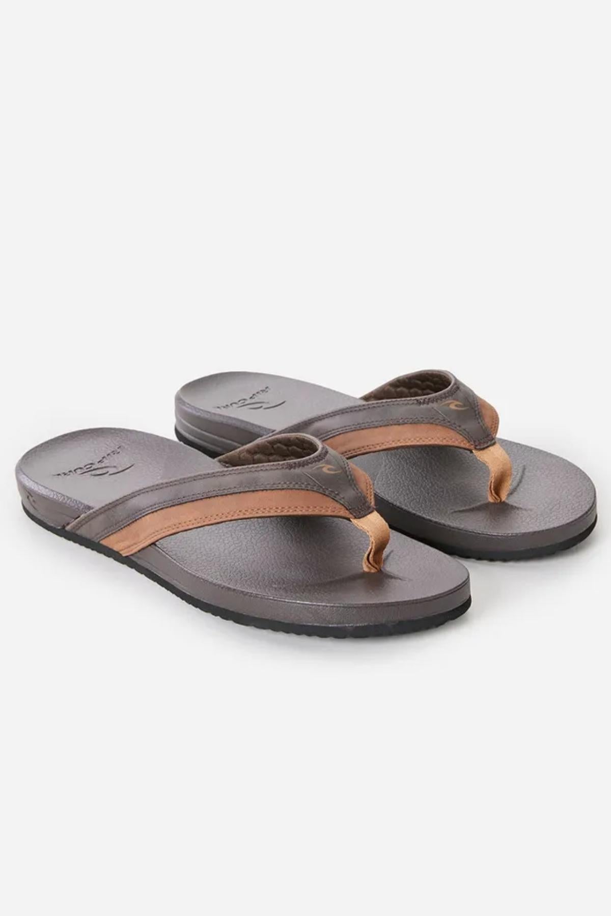 A pair of Rip Curl Soft Top Thongs featuring men's flip-flop sandals with grey soles and brown leather straps. These sandals have a simple, casual design suitable for everyday wear, with the brand logo visible on both the footbed and the straps. The background is plain white.