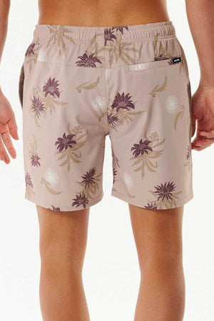 The person stands with their back to the camera, wearing Rip Curl Sun Razed Floral Volley board shorts. These stylish swim trunks feature a light floral pattern with brown and purple flowers on quick-dry fabric, an elastic waistband, and visible rear pockets against a plain, light background.