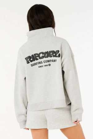 A person with long brown hair wears a light gray Rip Curl Surf Puff 1/4 Zip sweatshirt and matching shorts. "Rip Curl Surfing Company Since 1969" is boldly printed on the back as they face away, ready for adventure.