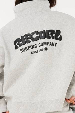 Someone wearing a light gray Rip Curl Surf Puff 1/4 Zip with "RIP CURL SURFING COMPANY SINCE 1969" in bold black print on the back—ideal for outdoor adventures. The person's face is not visible.