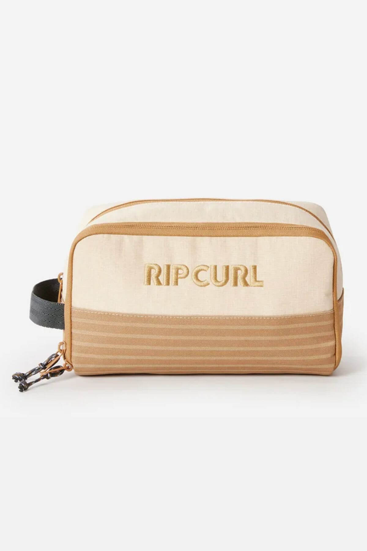 The Rip Curl Surf Revival Toiletry Bag in beige is crafted from recycled polyester and features brown accents along with a black side handle. The front showcases the embossed "Rip Curl" logo and a striped design at the bottom. The zipper has a black pull cord with a small decorative knot.