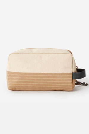 The Rip Curl Surf Revival Toiletry Bag is a two-tone beige and tan rectangular travel pouch featuring a black handle on one side. Crafted from recycled polyester, it boasts a simple design with a zip closure and includes a small fabric loop for hanging. The bottom portion is adorned with horizontal stripes.