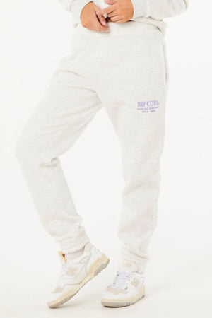 Wearing the Rip Curl Surf Staple Trackpant in light gray with purple text, paired with a matching sweatshirt and white sneakers, someone poses against a white background—ideal for relaxed, casual style.