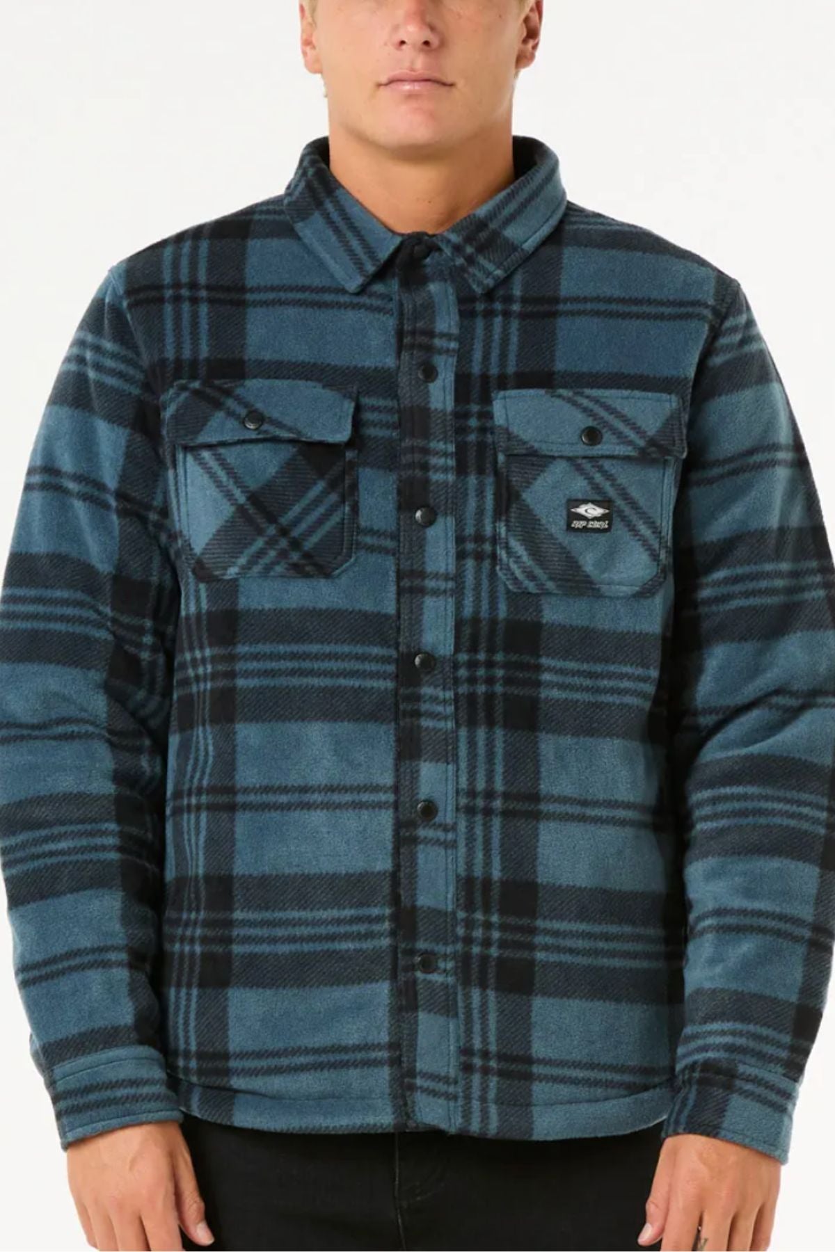 A person wears a Rip Curl Tofino Polar Fleece Jacket in blue and black plaid with chest pockets, made from recycled poly fleece, standing against a plain white background.