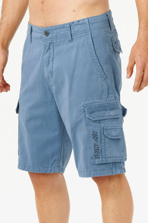 A man is wearing Rip Curl Classic Surf Trail Cargo Shorts in blue cotton with a relaxed fit, multiple pockets, button closure, decorative stitching, and an embroidered logo on the left pocket. Only his torso and legs are visible against a plain background.