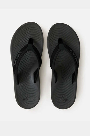 A pair of black Rip Curl Tunnels Bloom Thongs with textured eco-friendly BLOOM algae foam soles and "RIP CURL" branding on the straps and footbeds are displayed side by side on a white background.