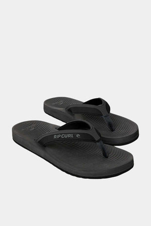 The Rip Curl Tunnels Bloom Thongs are black flip-flops with textured BLOOM algae foam footbeds and classic thong straps, shown on a plain white background.