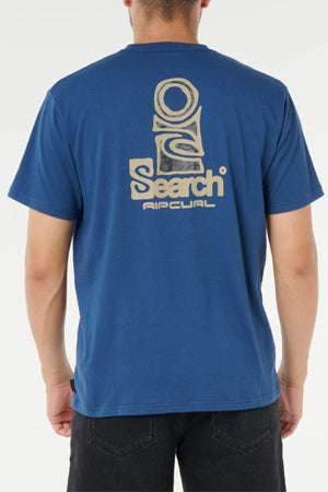 A person seen from the back wears a blue Rip Curl Vaporcool Search Stack Tee featuring a large abstract logo and "Search Rip Curl" in light beige on the upper back; this moisture-wicking t-shirt ensures cool comfort.