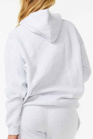 Someone in a Rip Curl Varsity Hoodie, light grey, paired with sweatpants, is facing away from the camera. The hoodie features long sleeves and a comfortable heritage fit with a hood made from cotton poly fleece, all set against a plain white background.