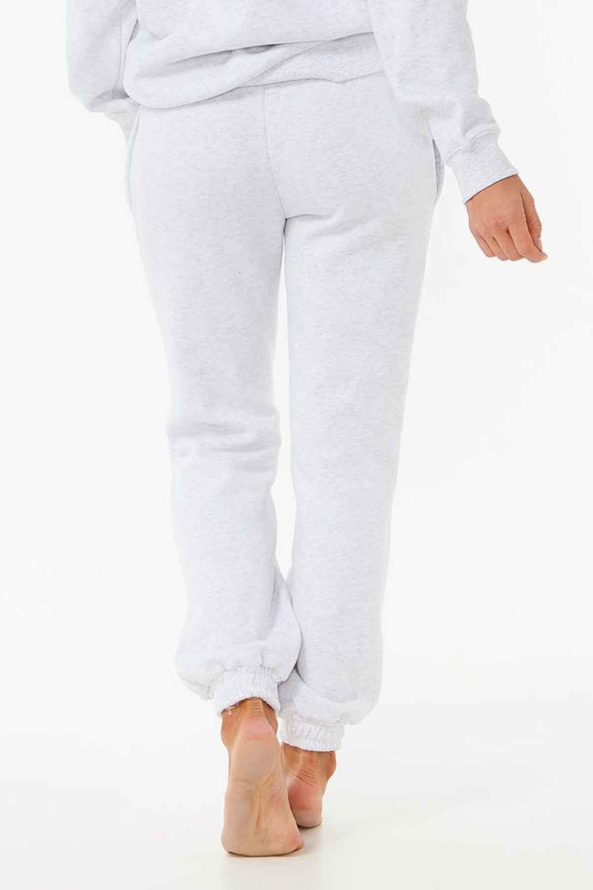 A person is shown walking away in light gray Rip Curl Varsity Pants, made from soft Cotton Poly Fleece with elastic ankle cuffs, perfect for casual wear, against a plain white backdrop.