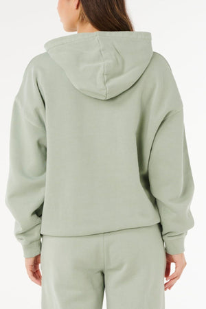 A person is shown from the back against a plain white background, wearing a light green Rip Curl Varsity Sports Oversized Hood and matching sweatpants.