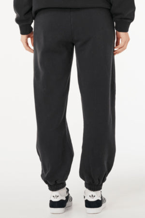 A person is shown from the back against a plain white background, wearing Rip Curl Varsity Sports Track Pant and black-and-white Adidas sneakers.
