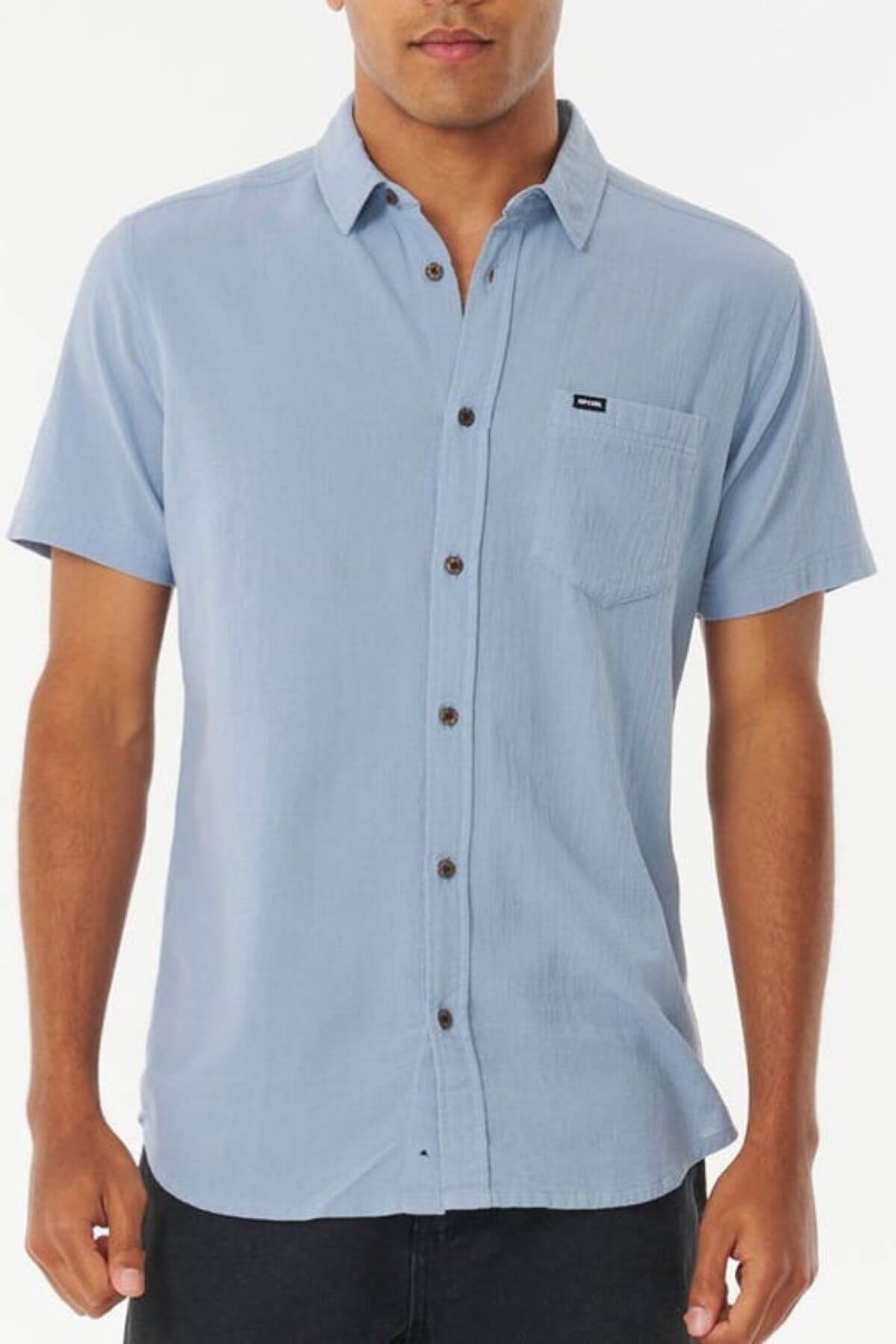 A man wearing the Rip Curl Washed Short Sleeve Shirt in light blue cotton with a front pocket, standing against a plain white background.