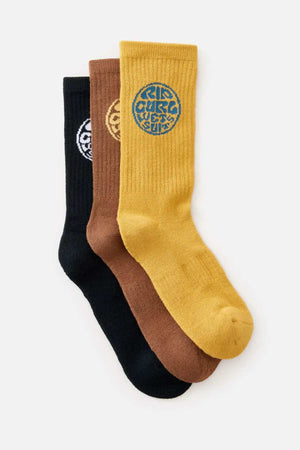 Three pairs of Rip Curl Wetty Crew Socks are shown in black, brown, and mustard yellow colors. Each sock features a circular woven design with intricate patterns near the top and offers ultimate comfort with arch support. The socks are neatly displayed against a plain white background.