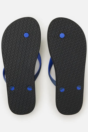 The image shows the bottom view of a pair of Rip Curl Wetty Fade Bloom Thongs, featuring black soles and blue straps. The soles have a textured pattern with three blue circular plugs visible on each thong, likely securing the straps to the sole. The background is plain white.