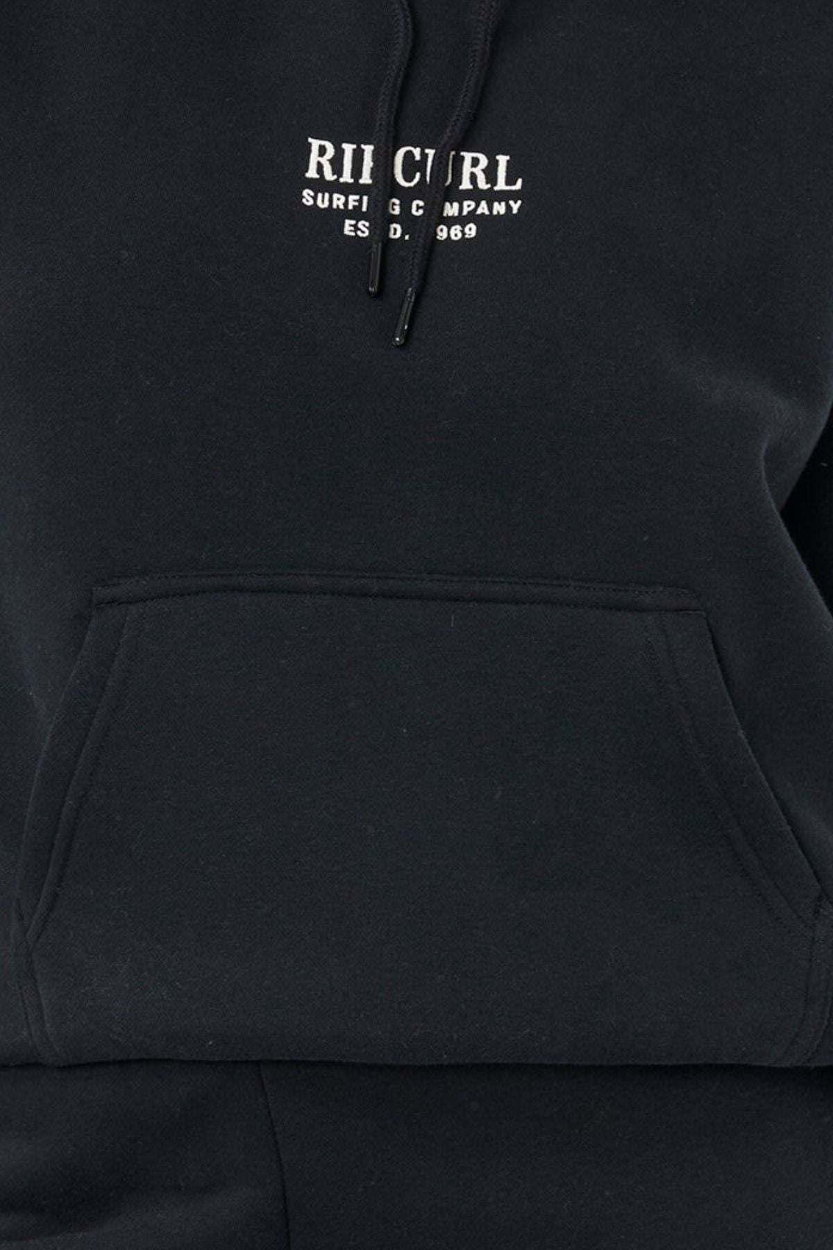 A close-up of the Rip Curl Surf Staple Relaxed Hood, a relaxed-fit hoodie with a front pocket and "RIP CURL SURFING COMPANY EST. 1969" in white on the chest, celebrating classic surf heritage.