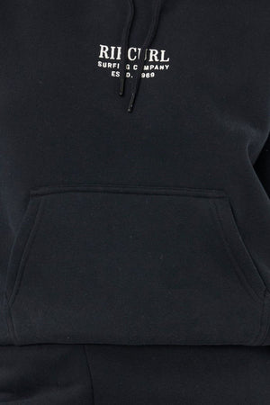 A close-up of the Rip Curl Surf Staple Relaxed Hood, a relaxed-fit hoodie with a front pocket and "RIP CURL SURFING COMPANY EST. 1969" in white on the chest, celebrating classic surf heritage.