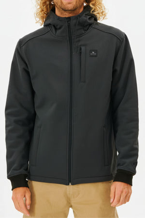 A person wears the Rip Curl Anti Series Soft Tech Fleece, a black zip-up hooded jacket with a chest pocket, paired with khaki pants, shown from the waist up against a plain background.