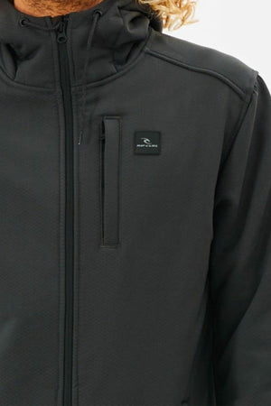 Close-up of a person wearing a black Rip Curl Anti Series Soft Tech Fleece jacket with hood and zippered chest pocket. The face is hidden, with blond hair visible on the right side.