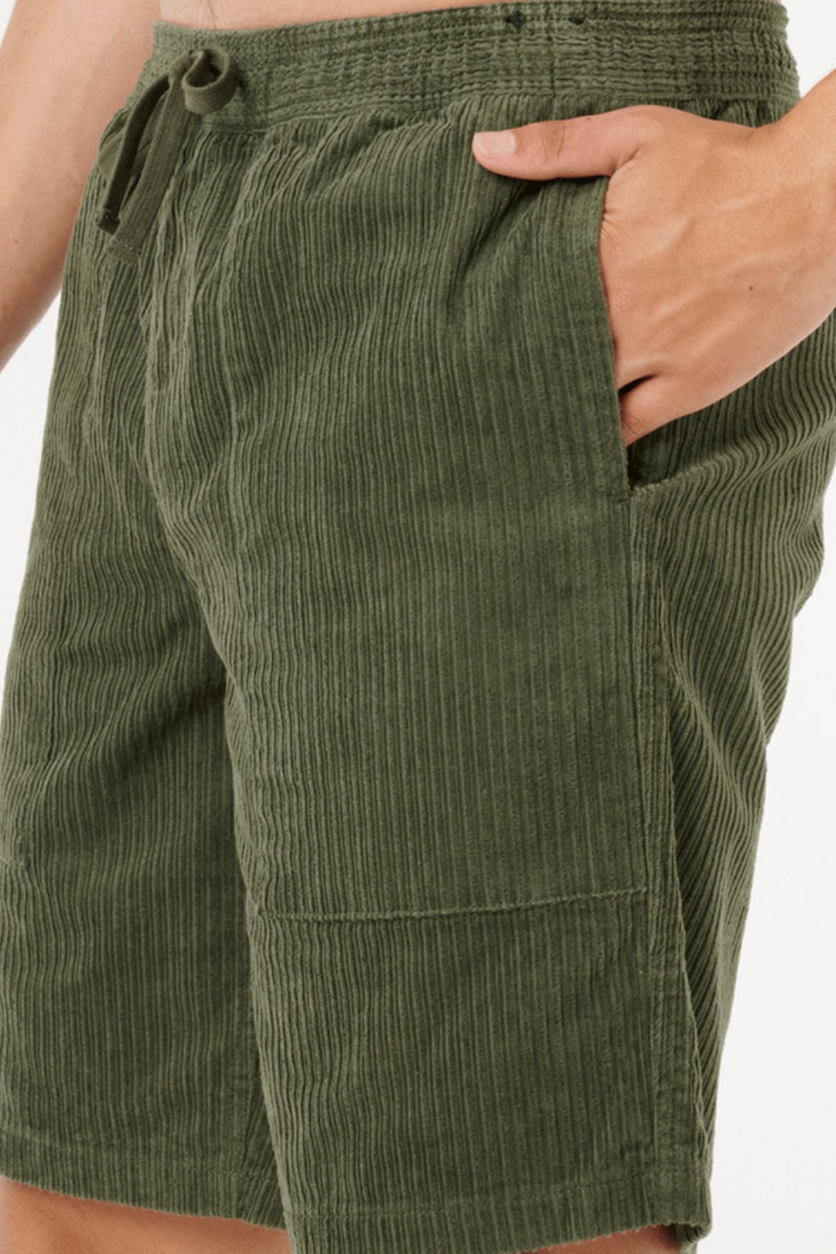 Someone wearing Rip Curl Classic Surf Cord Volley olive green cotton corduroy shorts, right hand in pocket, shown waist to mid-thigh against a white background, showcasing a vintage surf-inspired style.