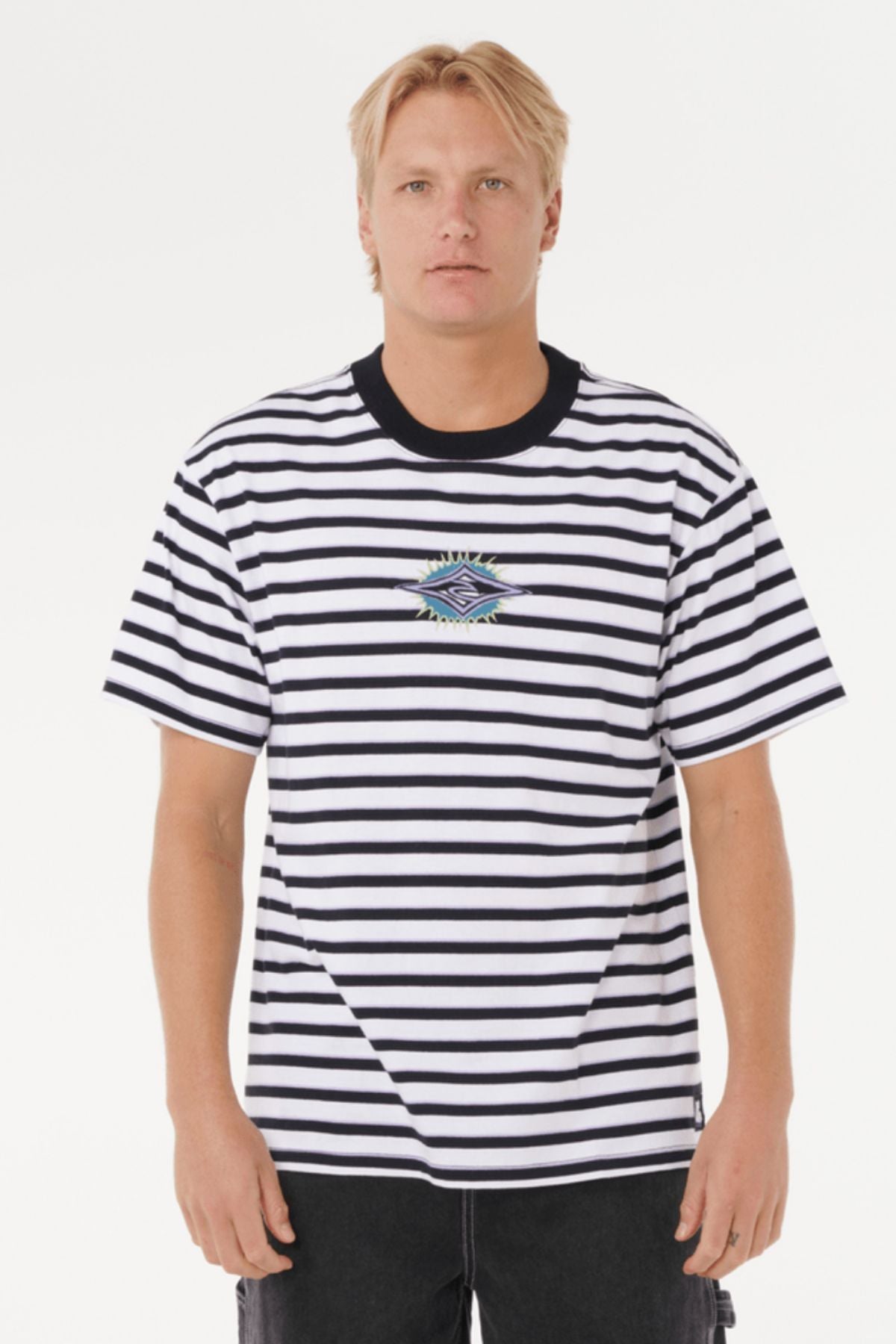 A blond-haired person wears a Rip Curl Raw Energy Stripey Tee, a black-and-white striped cotton jersey with an embroidered chest logo, standing against a plain white background.